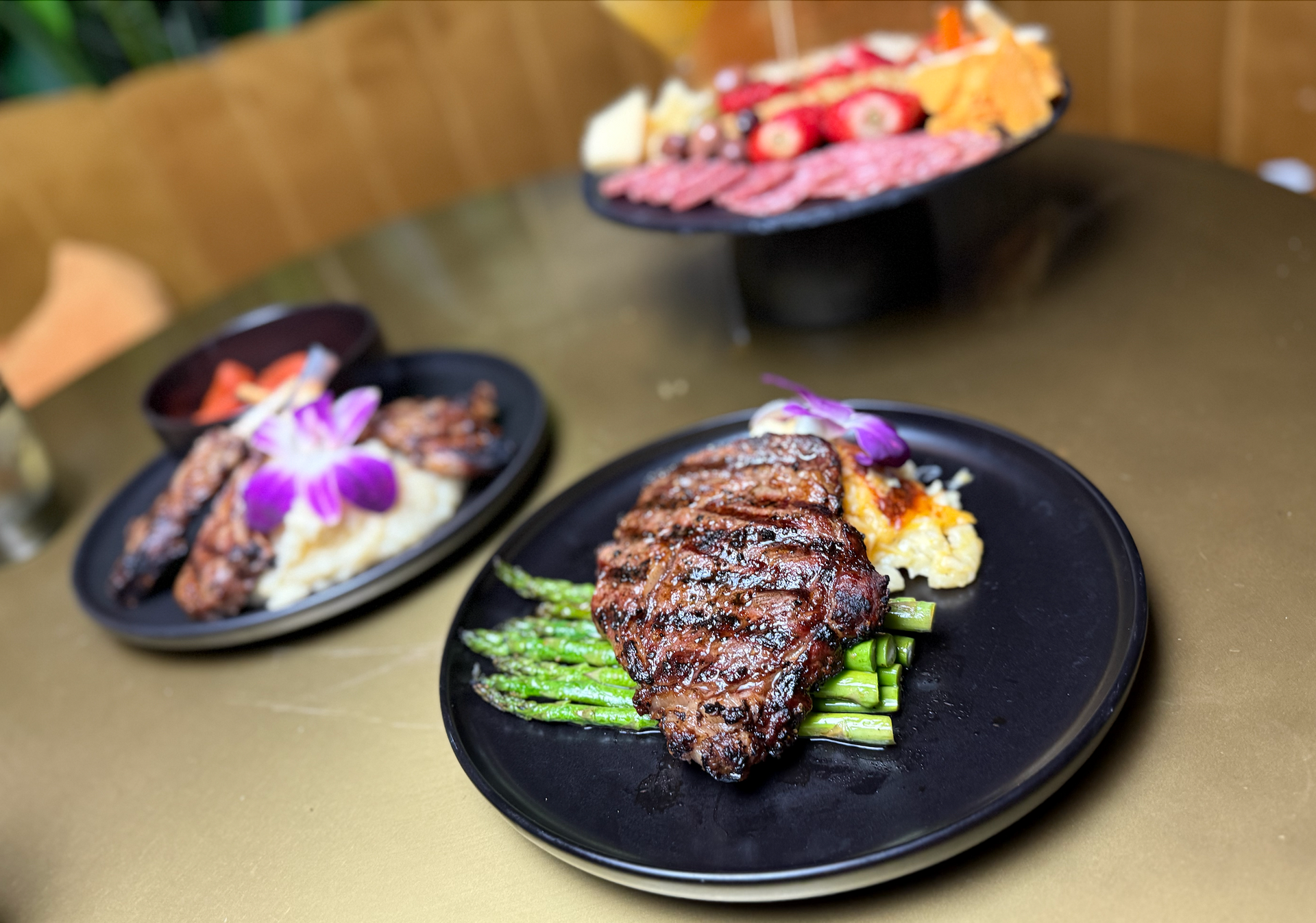 A steak with asparagus and mashed potatoes on a black plate on a table.