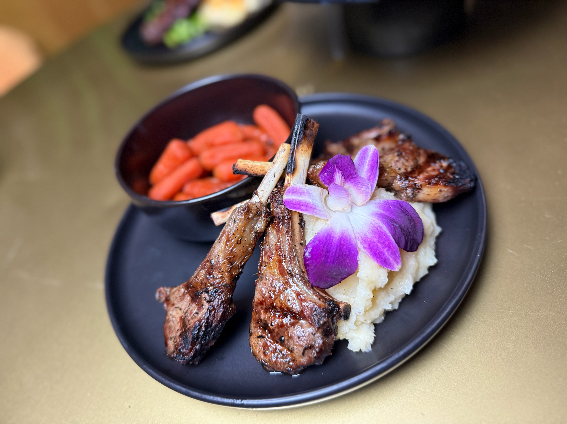 A black plate topped with lamb chops and mashed potatoes
