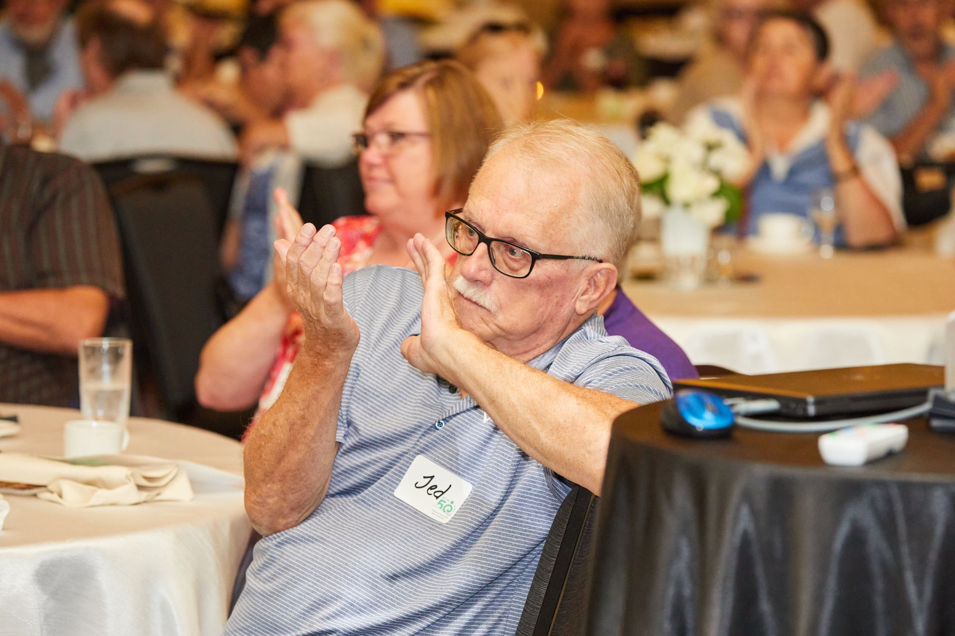 A man with glasses is sitting at a table clapping his hands.
