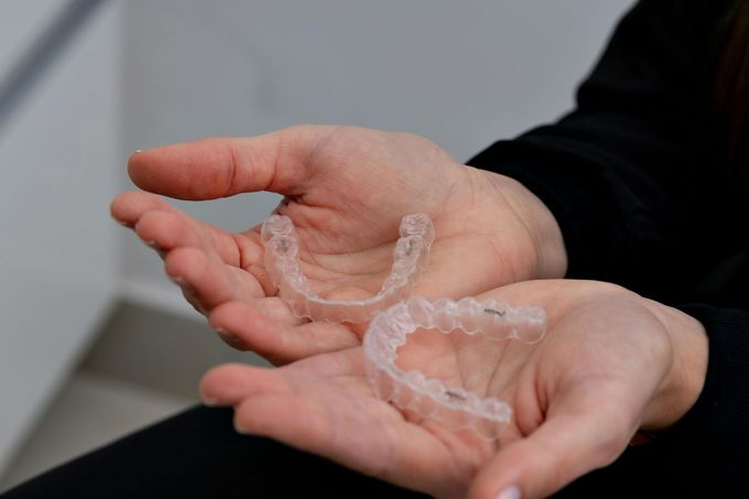 Hands holding two clear dental aligners.