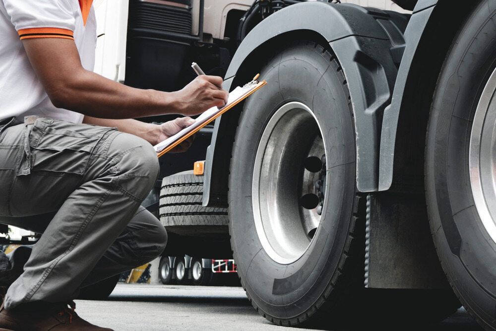 A Man Is Kneeling Down Next To A Truck And Writing On A Clipboard — A & D Automotive Technicians in Mackay, QLD