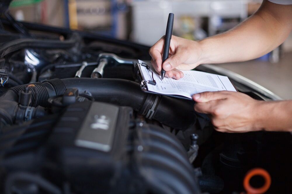 A Person Is Writing On A Clipboard Under The Hood Of A Car — A & D Automotive Technicians in Mackay, QLD
