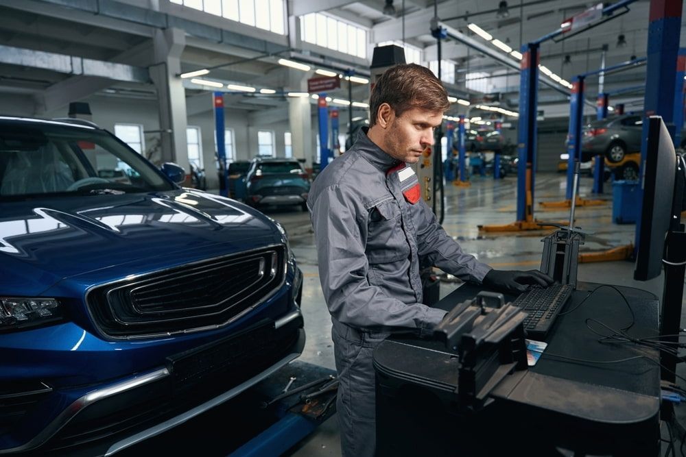 A Man Is Working On A Computer In A Garage Next To A Car — A & D Automotive Technicians in Mackay, QLD