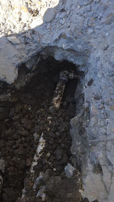 Close-up of a small pipe or rod embedded in a cracked concrete hole with dirt around it