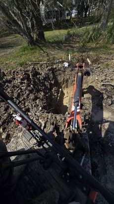 Excavators digging a deep trench in a grassy wooded area