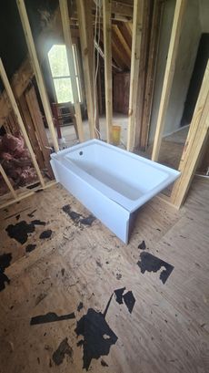 White bathtub in an unfinished room with exposed studs and plywood subfloor