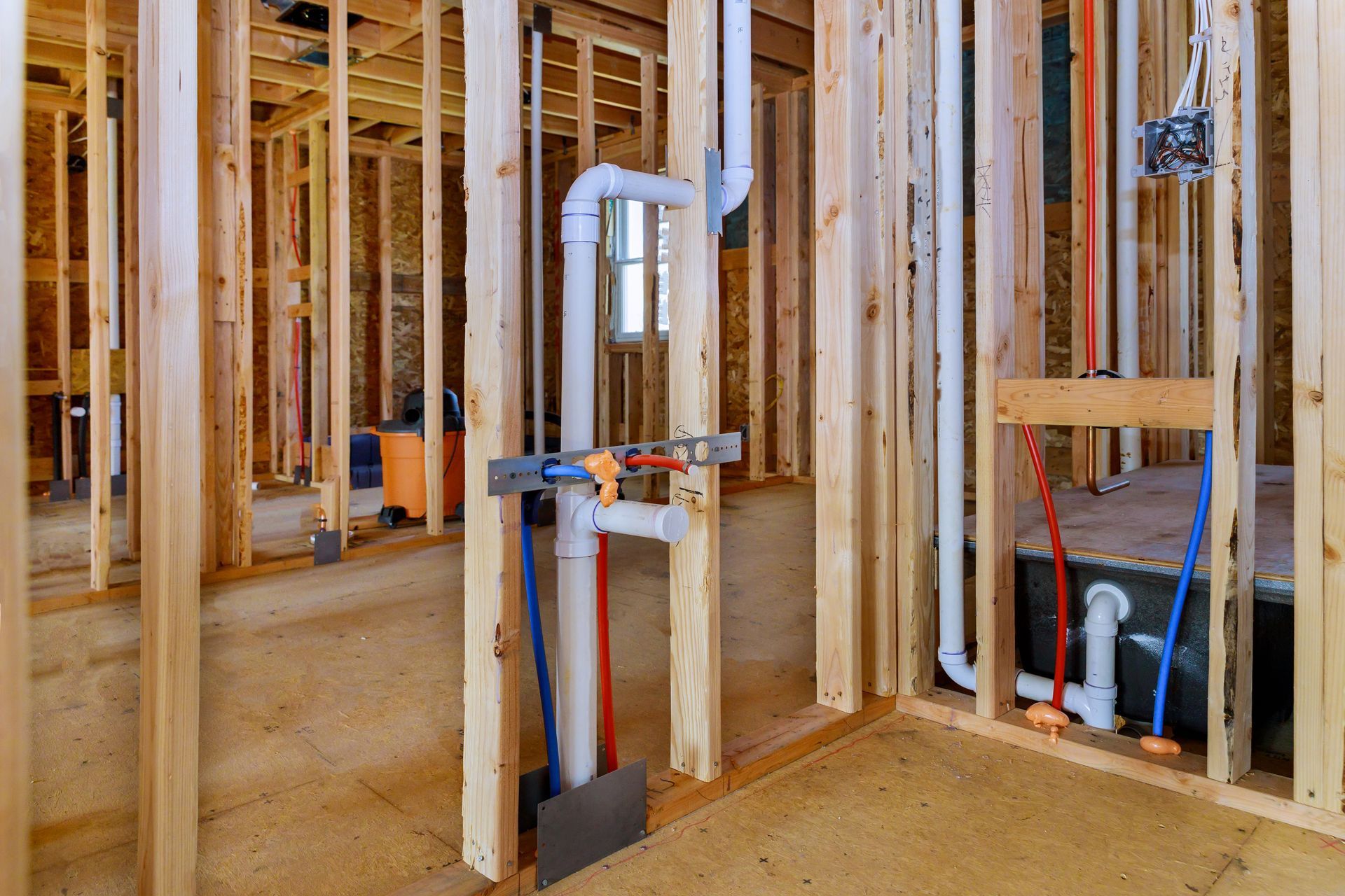 Unfinished house framing with exposed plumbing, pipes, and electrical wiring inside wood stud walls