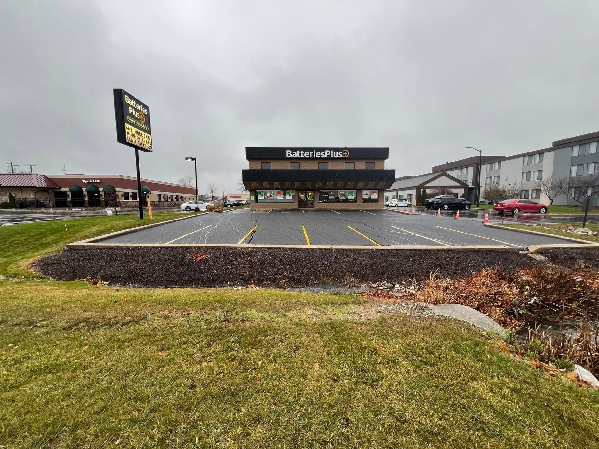 Gas station parking lot with EV charging spaces and a road sign under overcast sky