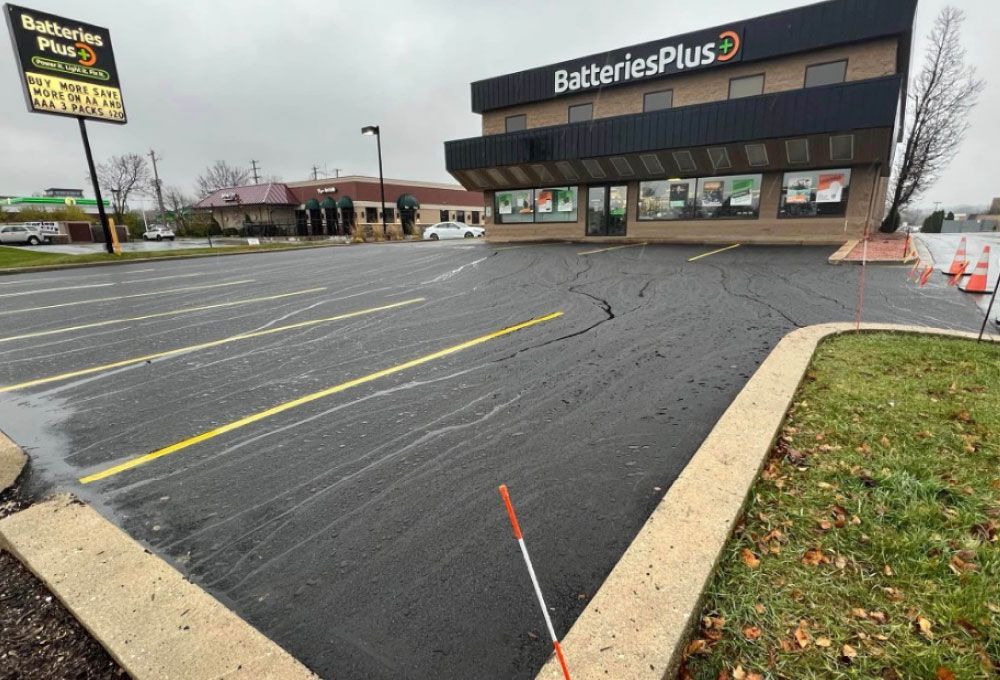 Batteries Plus storefront with an empty asphalt parking lot and overcast sky