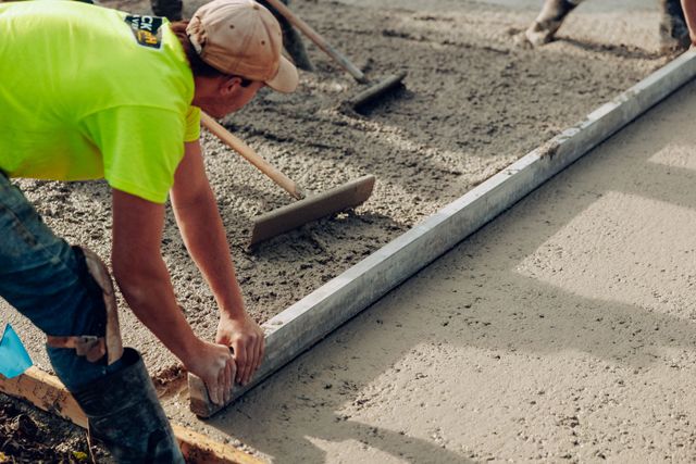 Worker smoothing wet concrete along a curb during sidewalk construction