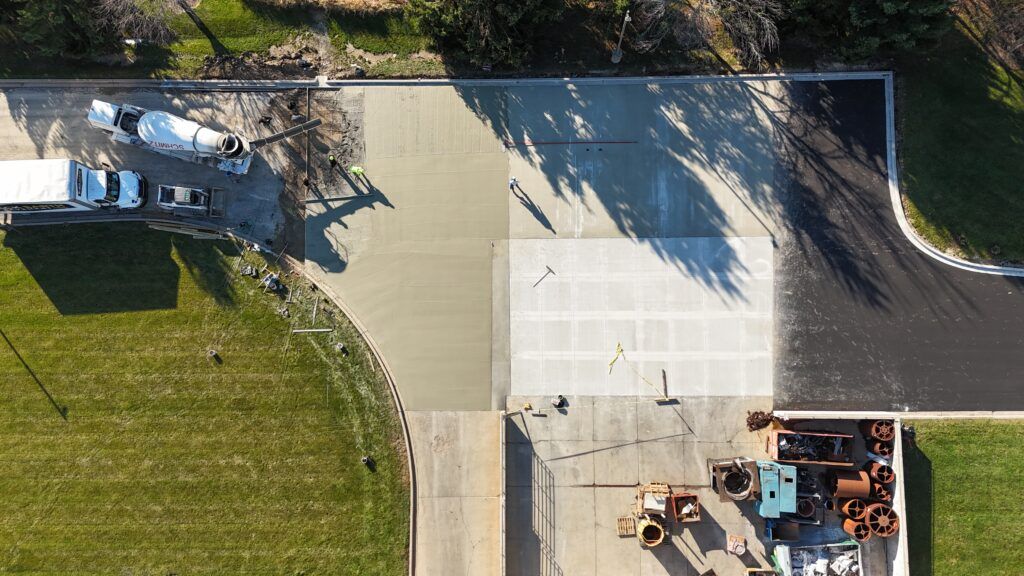 Aerial view of a concrete lot beside grass, with parked trucks and construction equipment under trees.