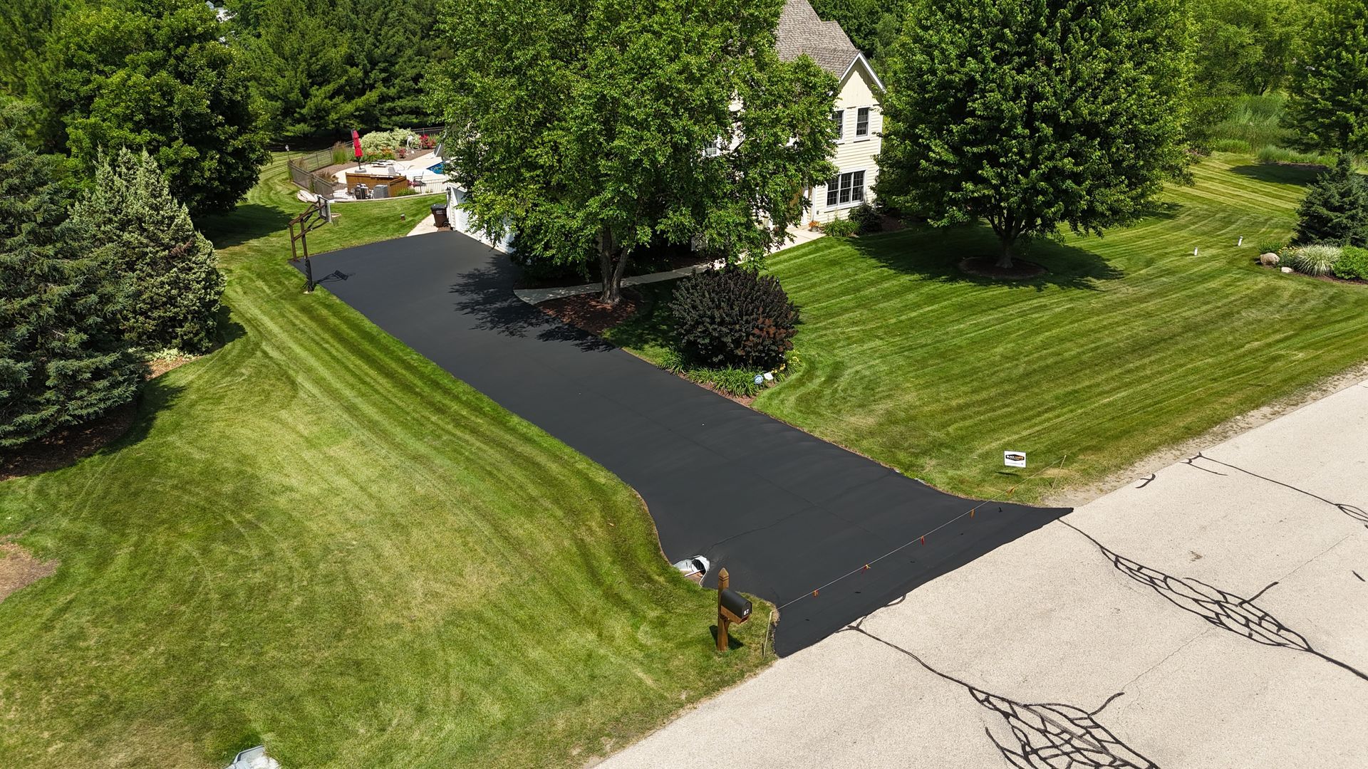 Fresh black asphalt driveway newly paved beside a green lawn and trees in a suburban yard.