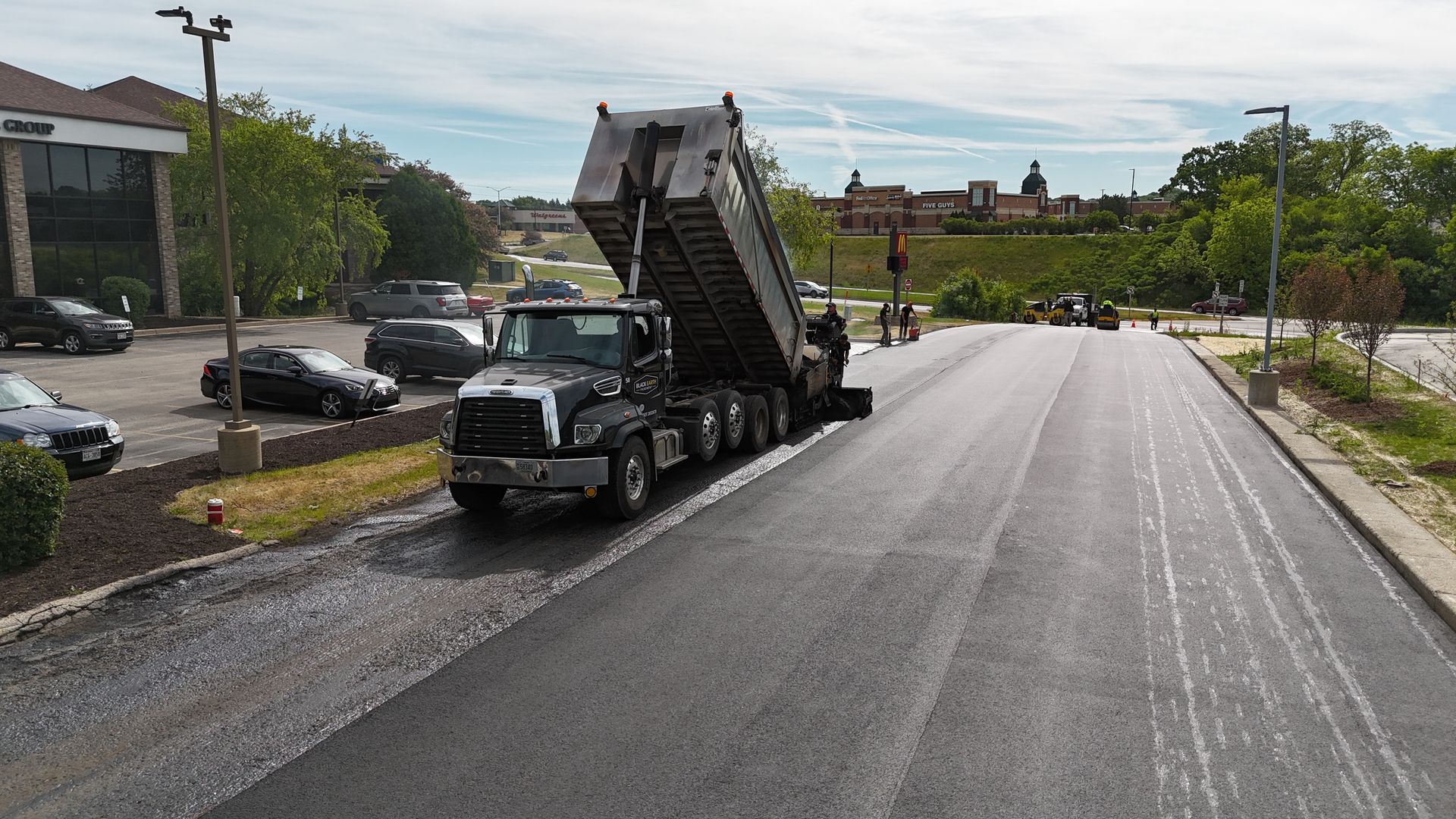 Black car carrier truck loading vehicles on a wet road near parked cars and trees