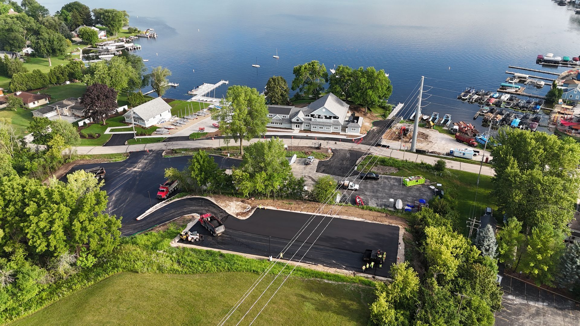 Aerial view of a lakeside park with a road, docked boats, and a parking lot beside the water