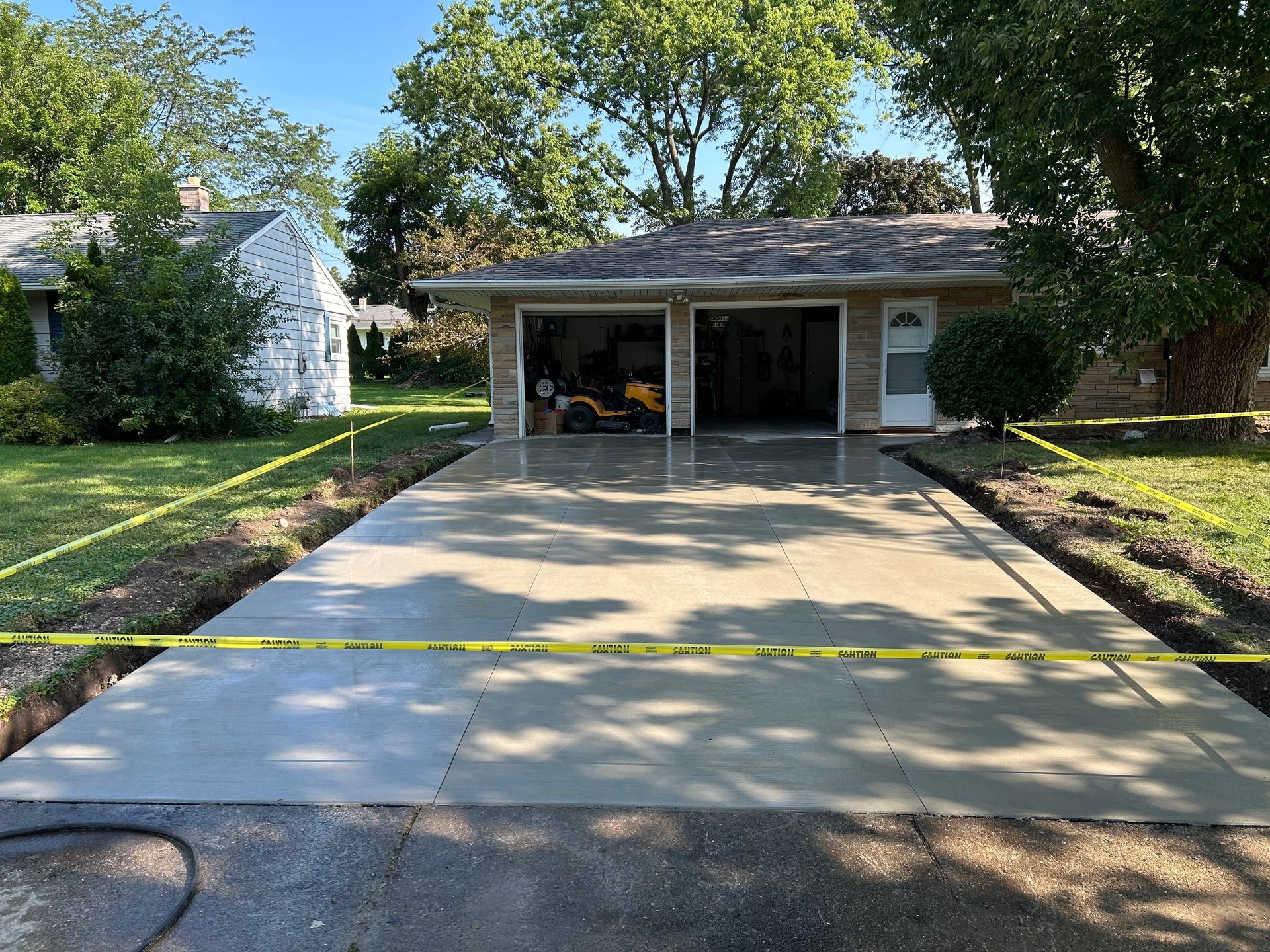 Driveway leading to a two-car garage with open bays, a concrete apron, and yellow caution tape across the front.