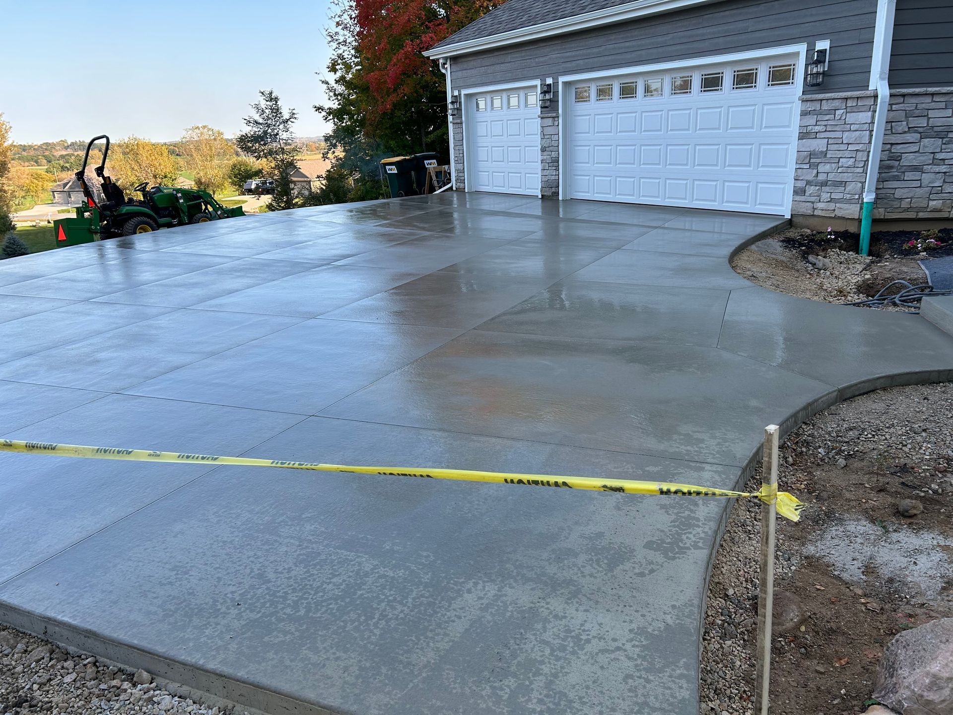 Fresh concrete driveway in front of a two-car garage, with yellow caution tape across the foreground