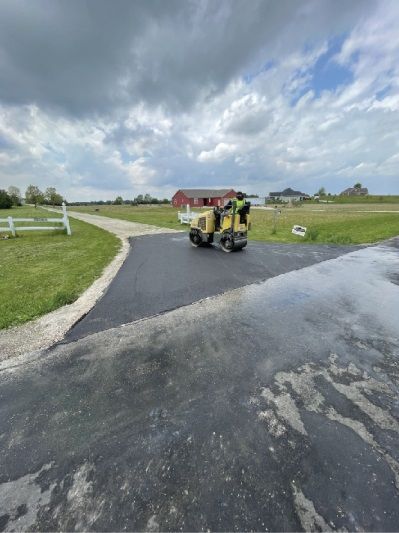 Workers in yellow vests paving a wet rural road under a cloudy sky