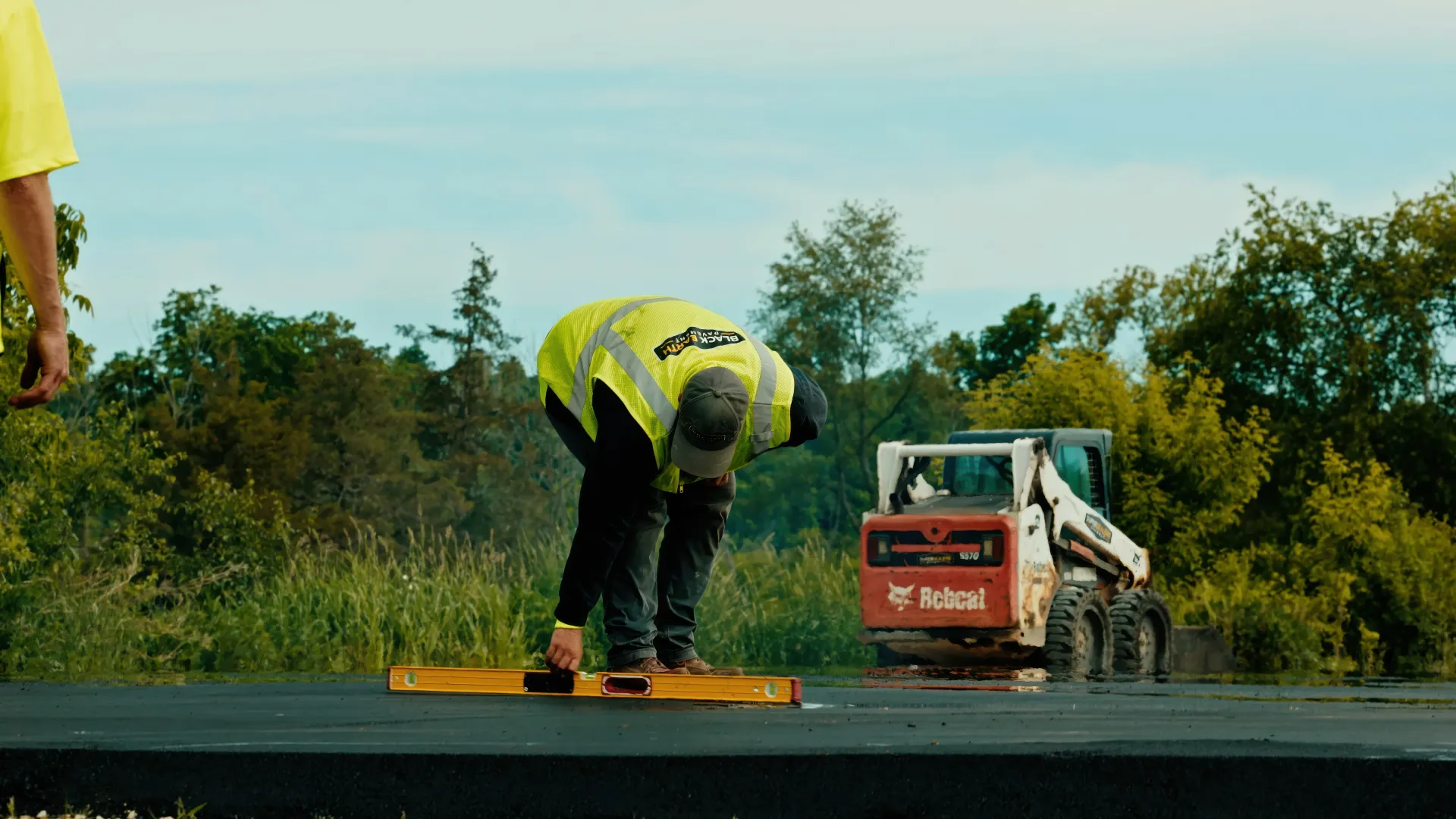 Aerial view of a freshly paved driveway beside a rural home, with paving equipment and a  truck nearby.