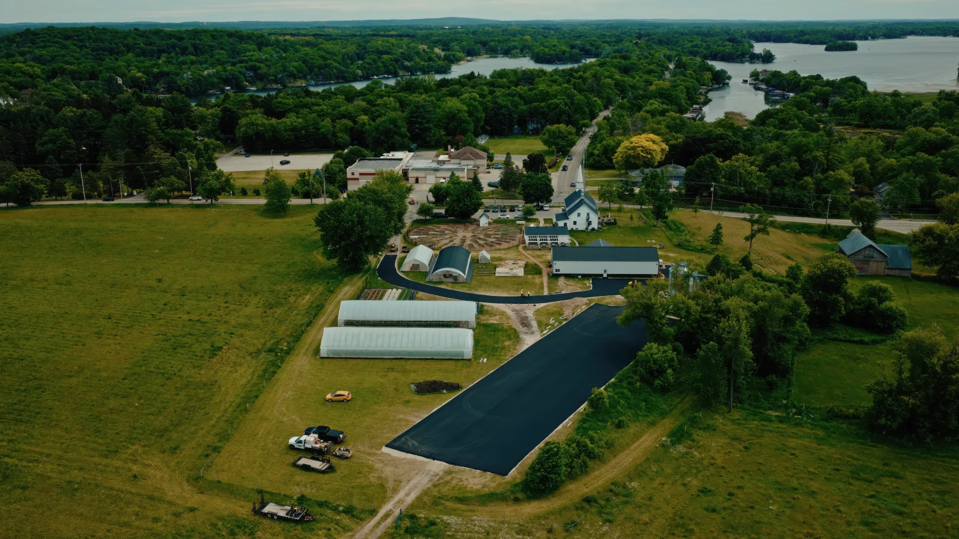 Aerial view of a rural farm with green fields, barns, and a small road leading to a tree-lined settlement.