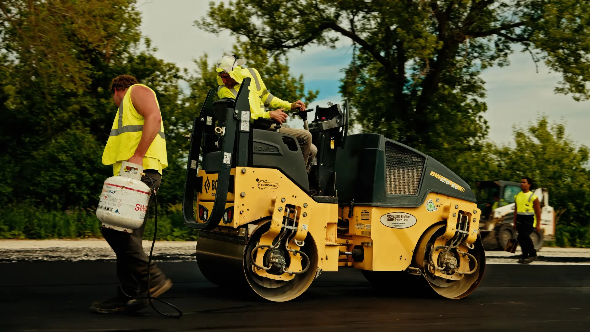 Road crew operating an asphalt paver beside a dump truck during a paving project.