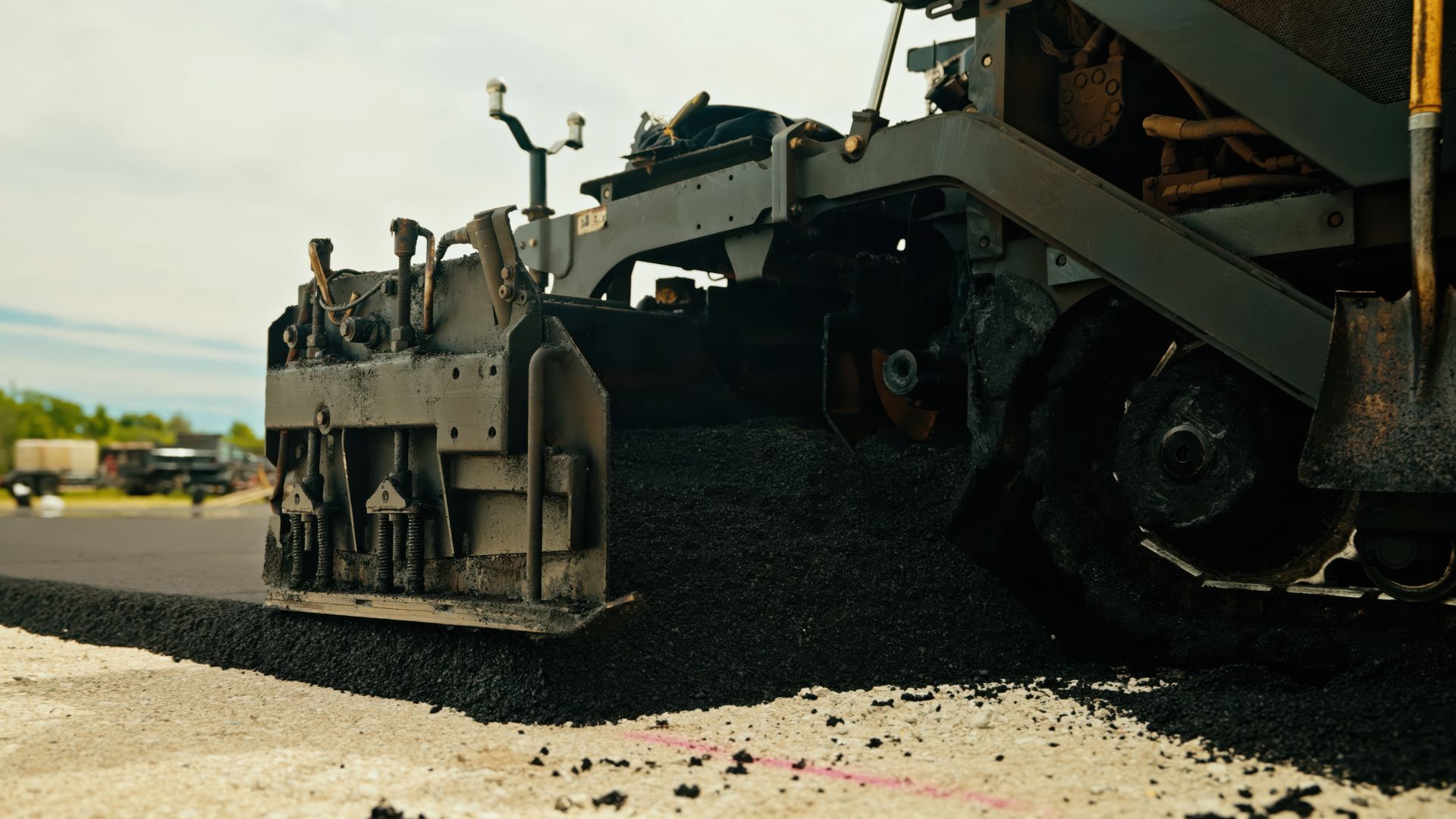 Black paving company dump truck parked outdoors with the driver visible inside the cab.