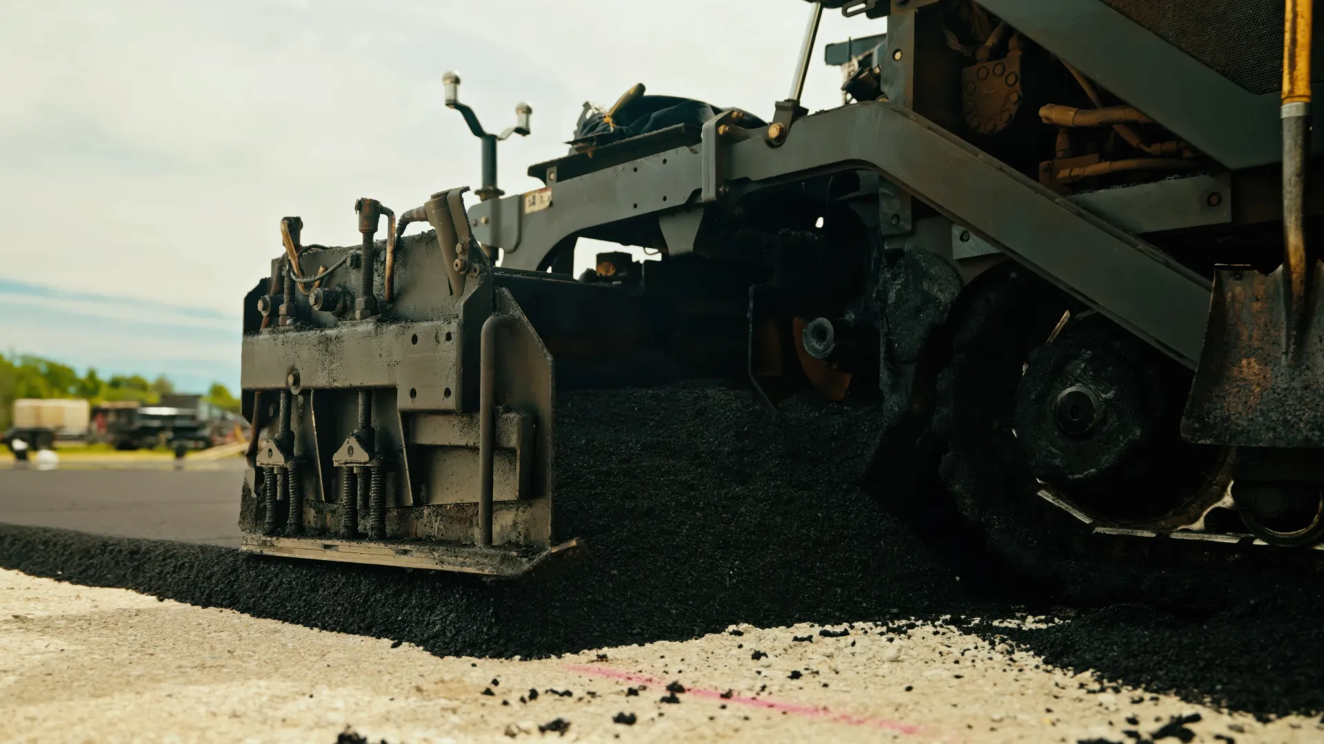 Road crew operating an asphalt paver beside a truck during a paving project.