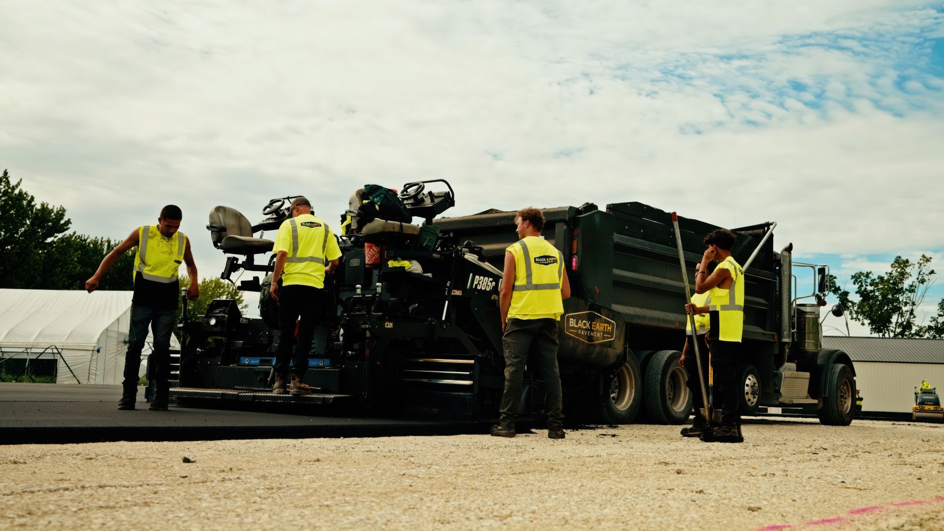 Workers in yellow safety vests stand beside a loaded truck at a construction site.