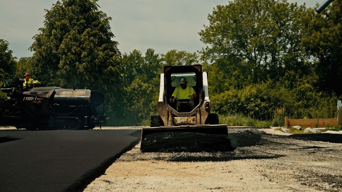 Road roller paving a black asphalt road on a sunny rural worksite