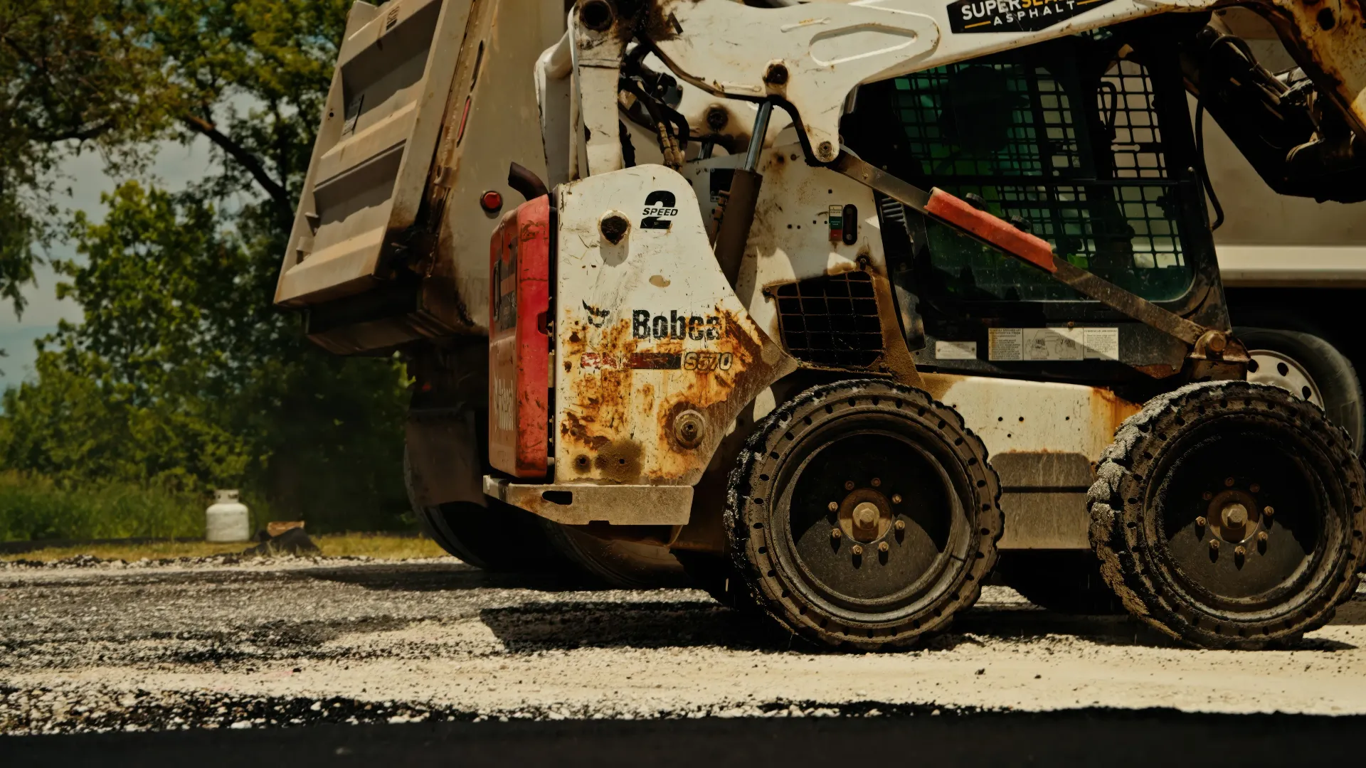Road crew operating an asphalt paver beside a dump truck during a paving project.