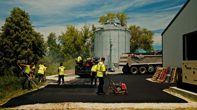 Workers in yellow vests around a grain silo and truck at a construction site.