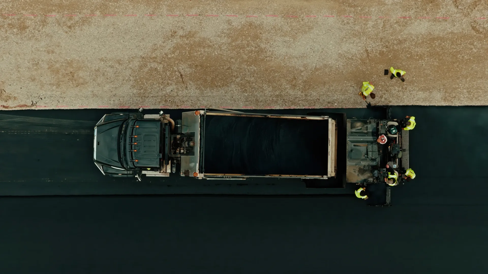 Black paving company dump truck parked outdoors with the driver visible inside the cab.
