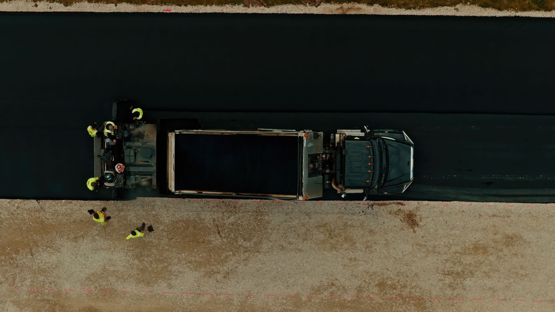Black paving company dump truck parked outdoors with the driver visible inside the cab.