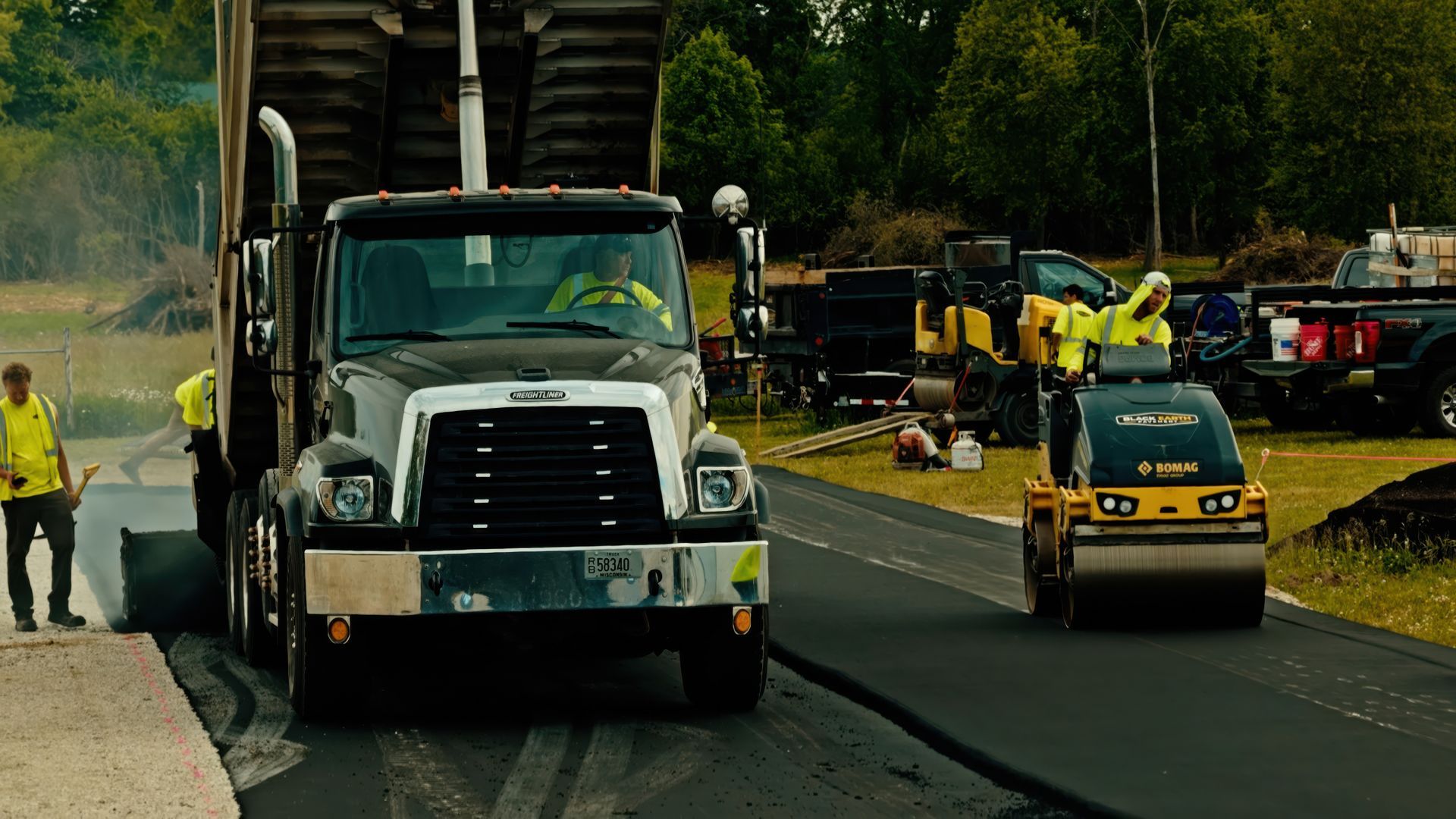Construction crew with a truck and road roller paving a road under a bridge.