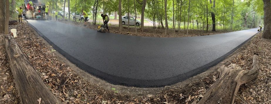 Panoramic view of a paved park path with trees, leaves, and a few people in the distance