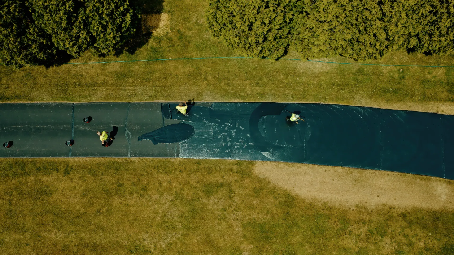 Aerial view of people canoeing on a narrow blue river between grassy banks and dense green trees
