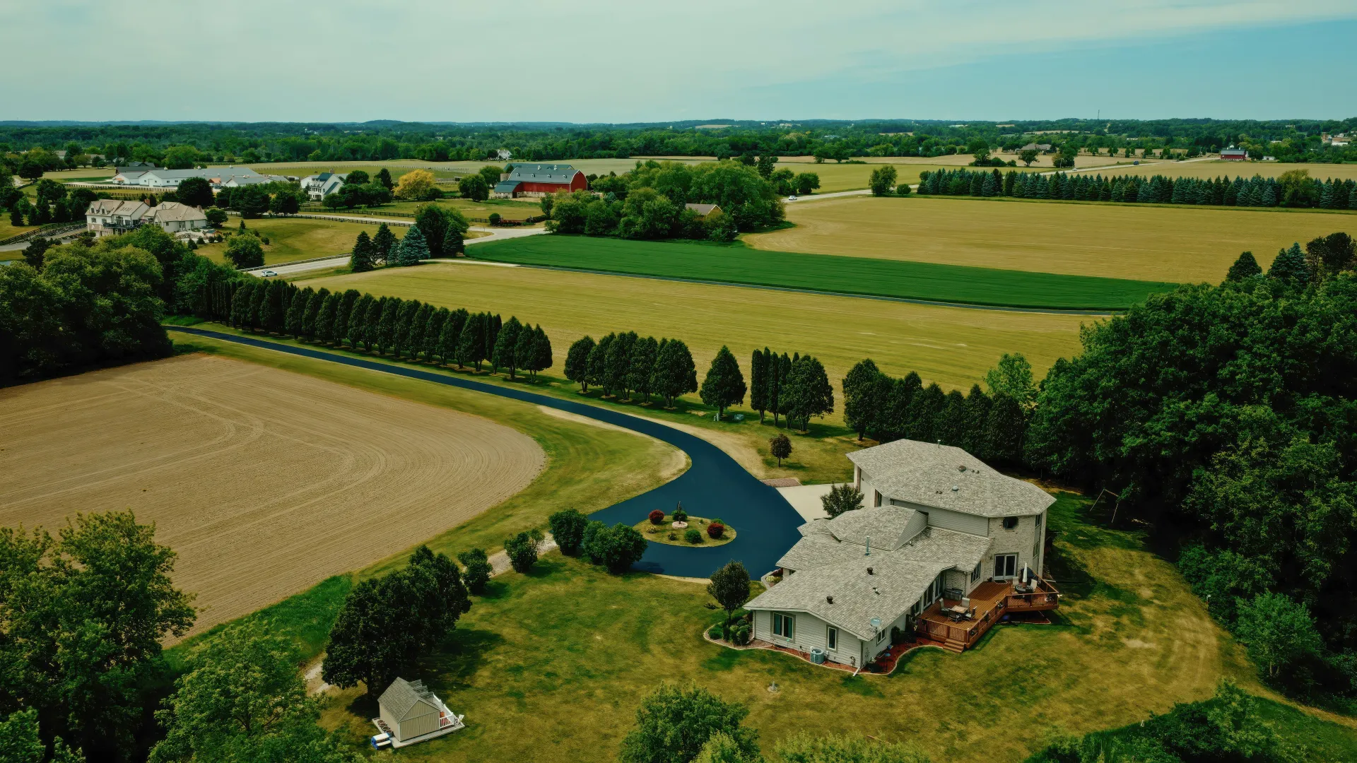 Aerial view of a farmhouse beside fields and winding road in a rural landscape