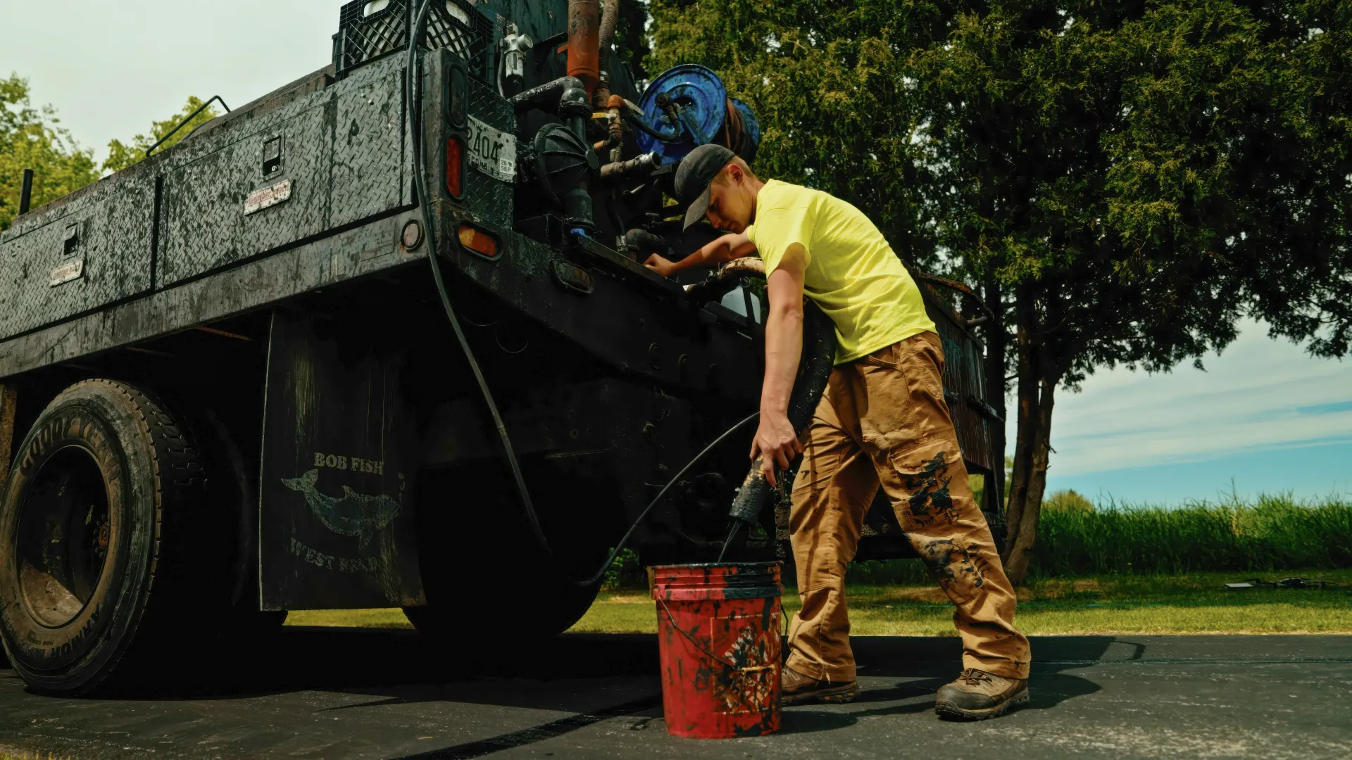 Aerial view of a freshly paved driveway beside a rural home, with paving equipment and a truck nearby.