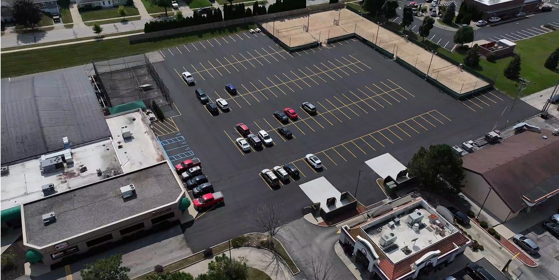 Aerial view of a parking lot beside buildings, with many parked cars and marked spaces