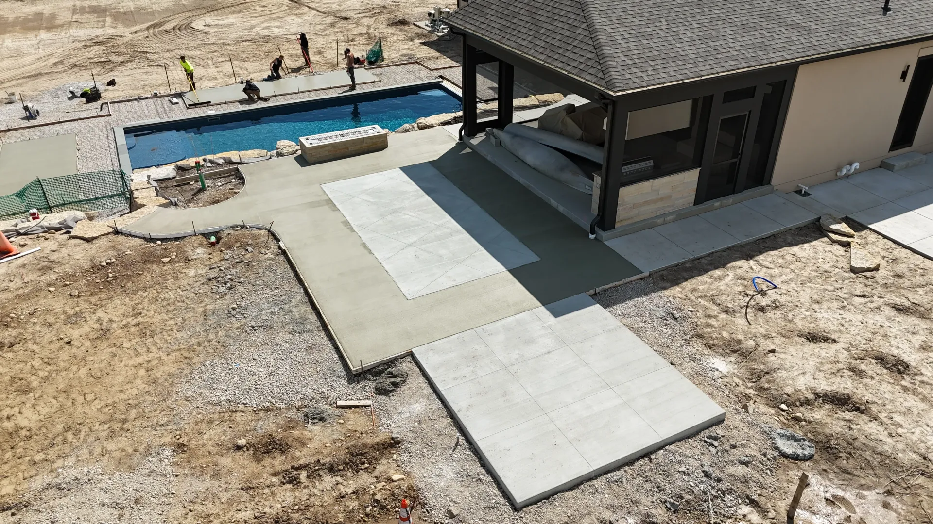 Concrete patio beside a pool and covered patio on a gravel yard under construction.