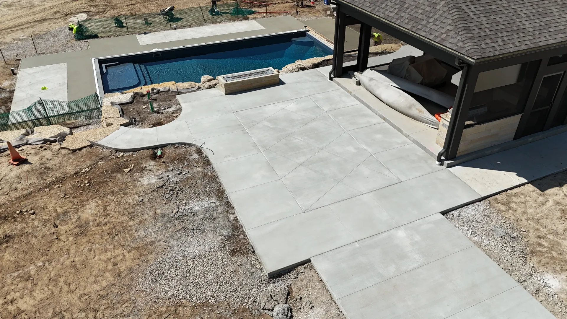 Concrete patio and walkway beside a house, leading to a covered area near a small blue pool.