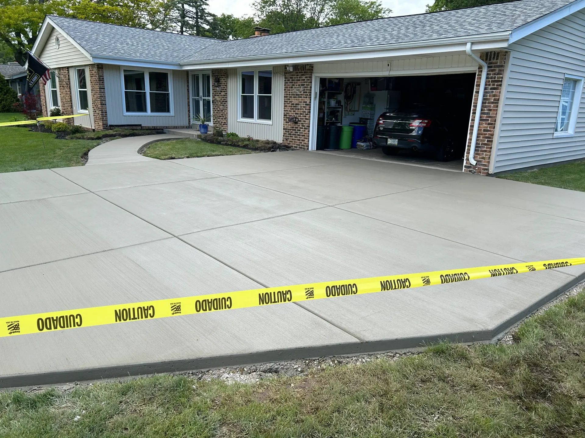 Yellow caution tape across a driveway in front of a house with an open garage and car inside