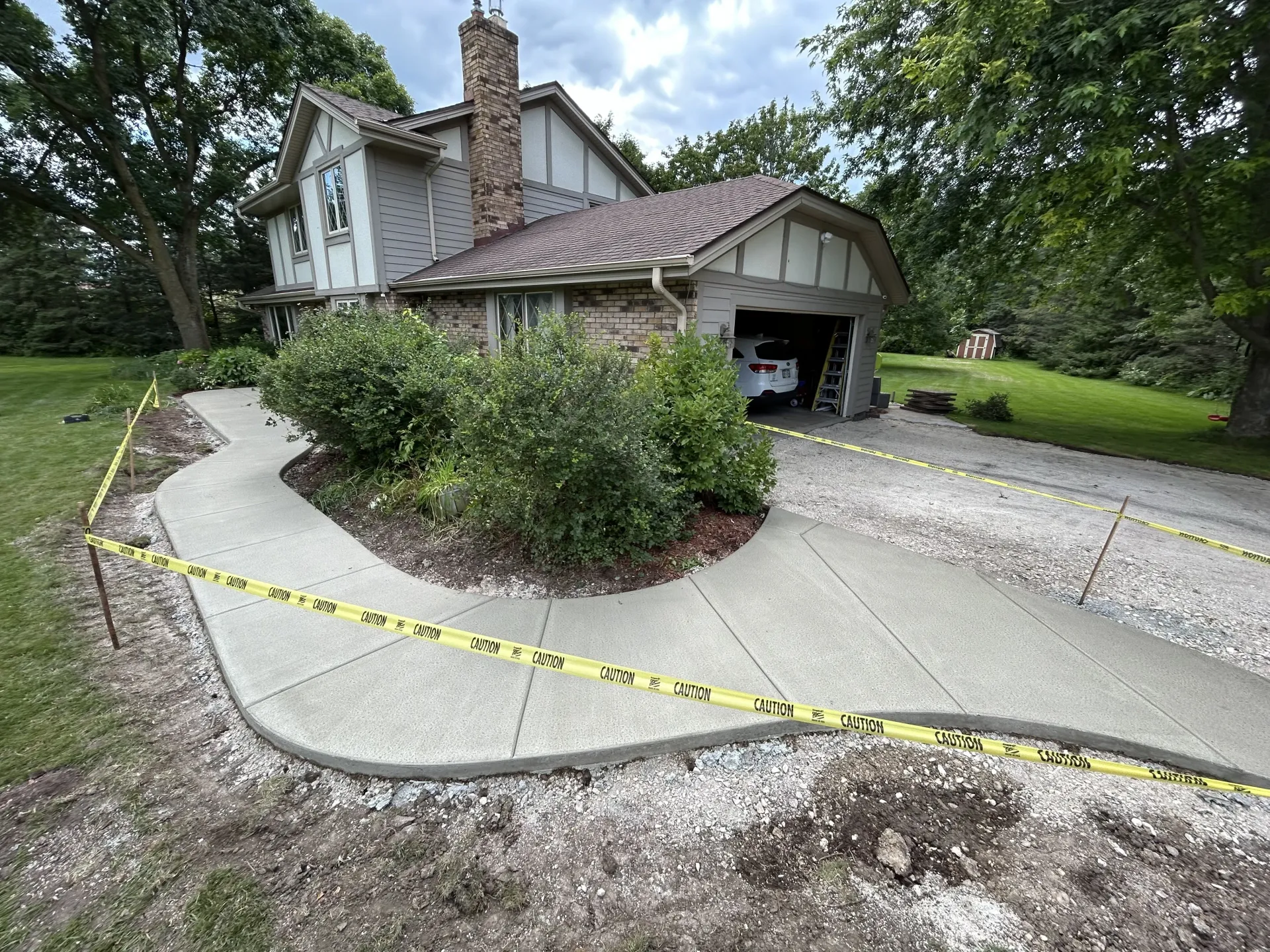 Damaged driveway and garage entrance blocked by yellow caution tape beside a house