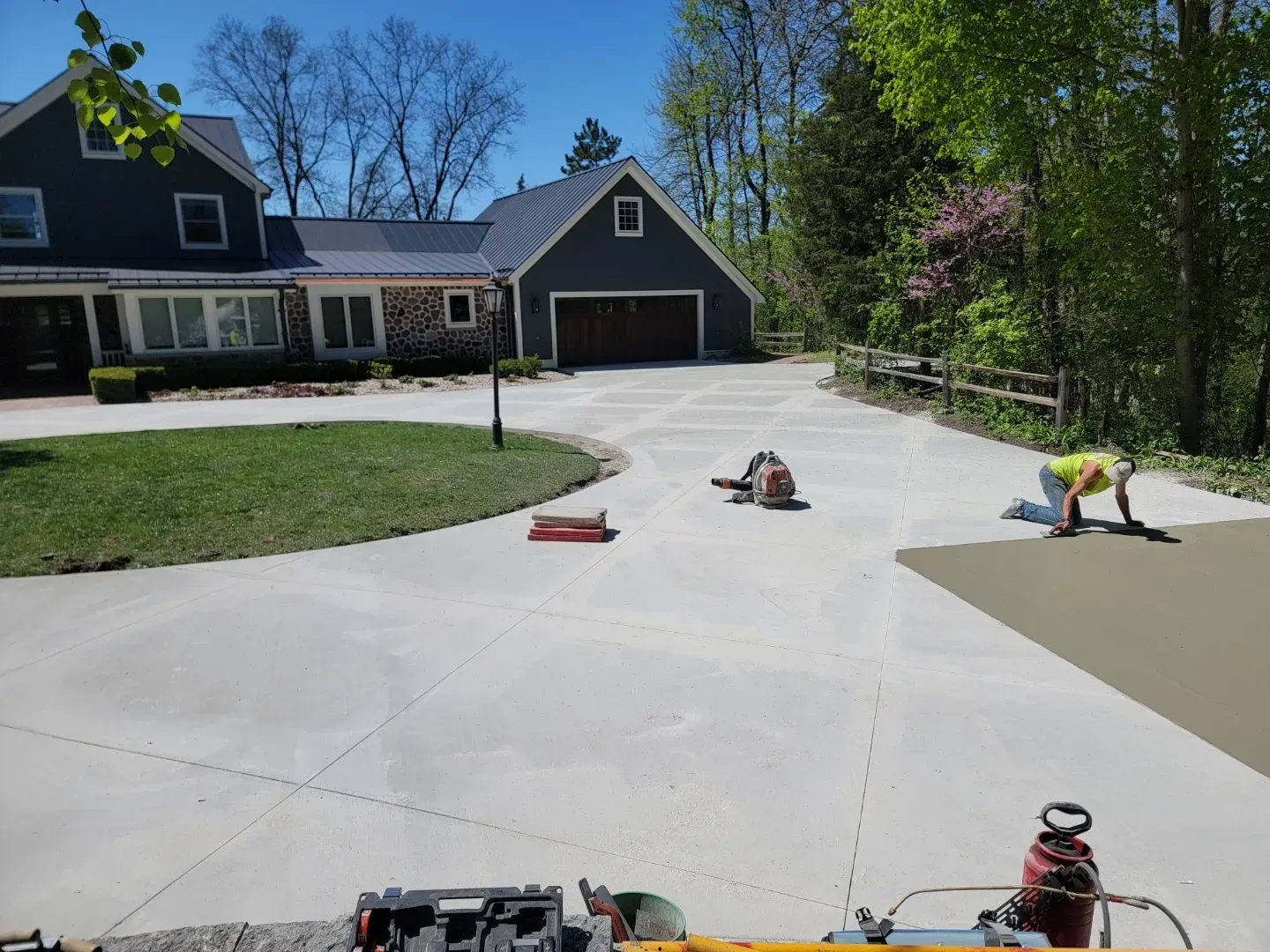 Large driveway in front of a house and garage, with scattered yard tools and supplies on the concrete.