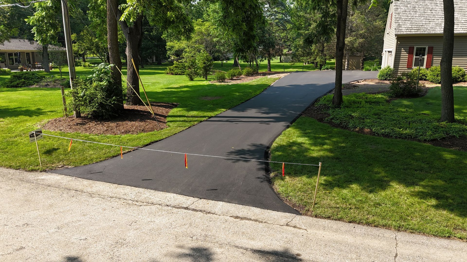 Two construction workers operating compact rollers on freshly paved asphalt near an industrial building.