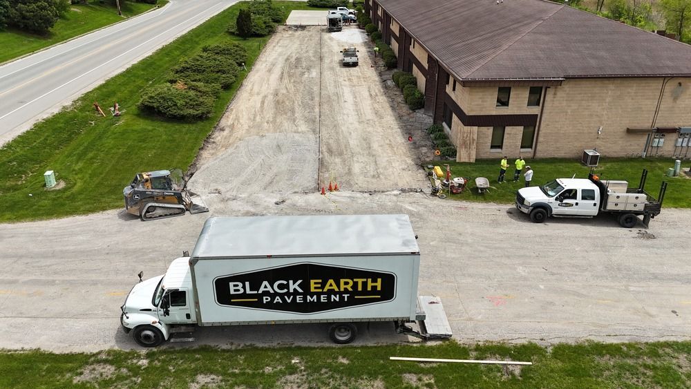 Aerial view of a Black Earth Moving truck parked outside a long building on a gravel lot.