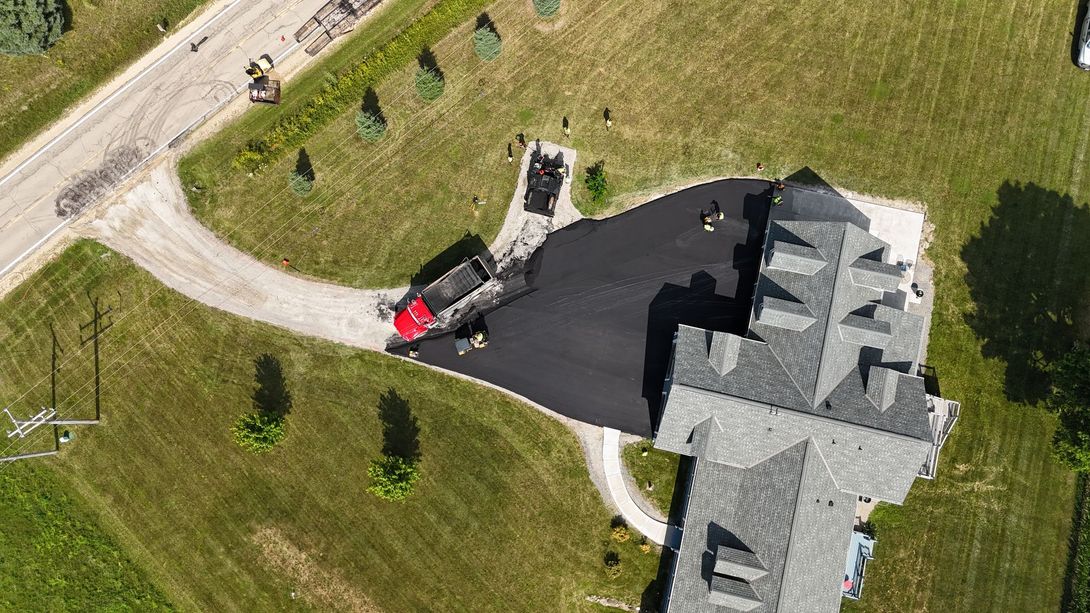 Aerial view of a house driveway with a red truck parked near a large gray-roofed home.