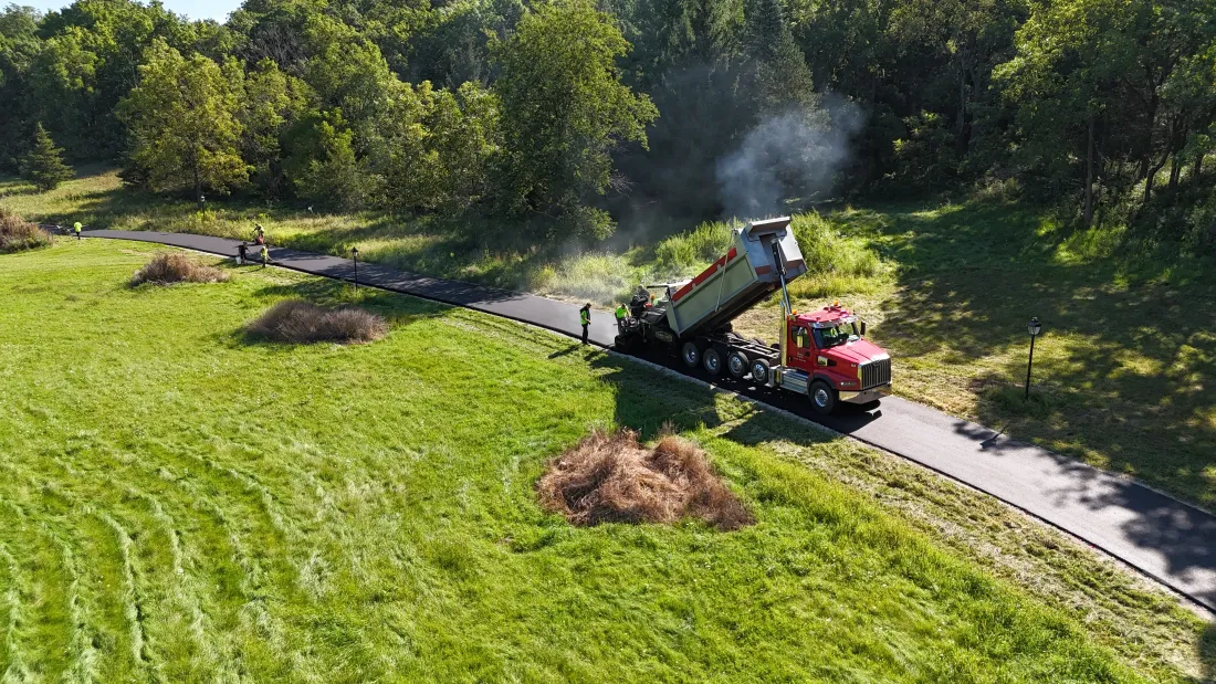 Red wood chipper on a path near a grassy field, blowing smoke as it processes branches and debris.