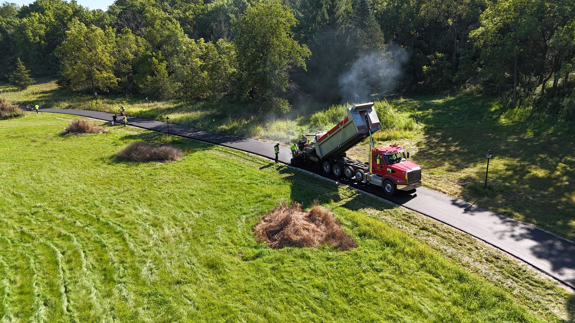Red truck operating a brush chipper along a path beside a green field, with a plume of smoke.