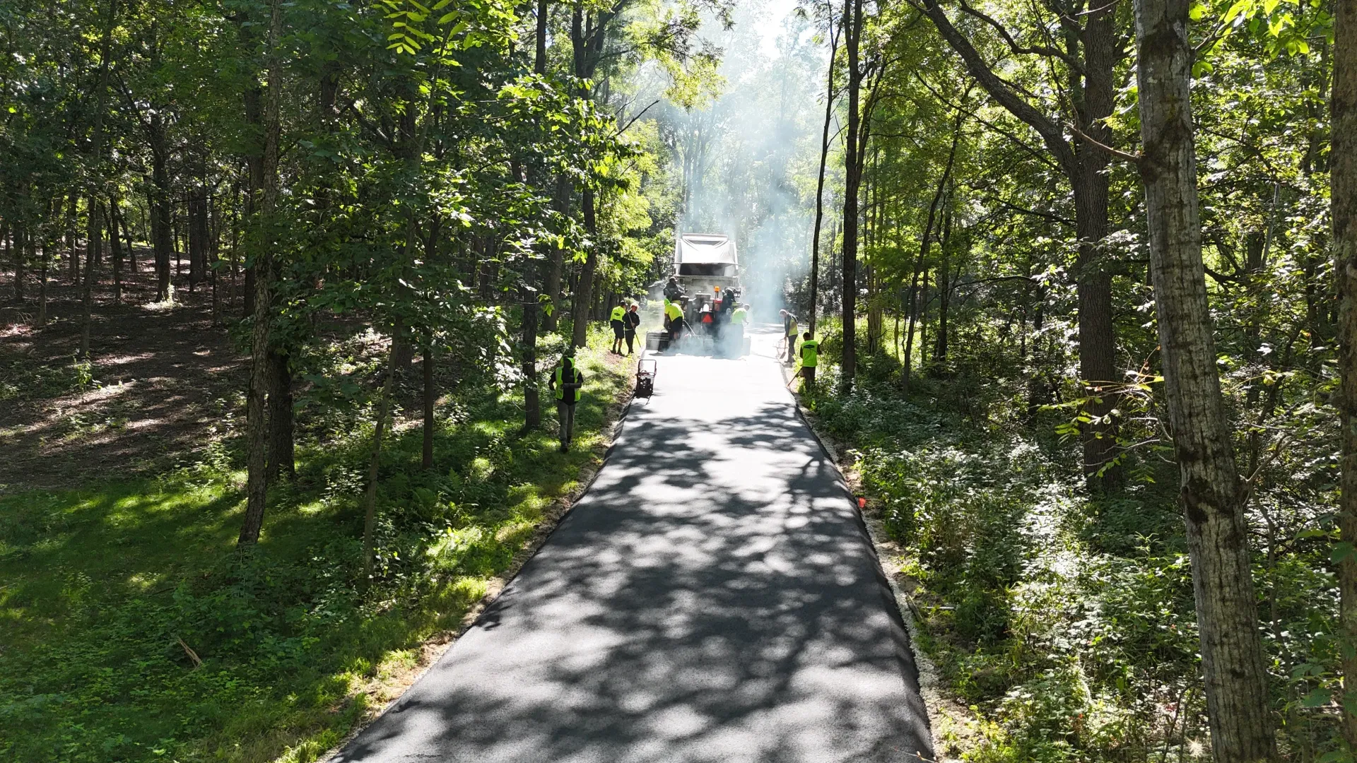 Tree-lined paved path leading to a small vehicle in bright sunlight
