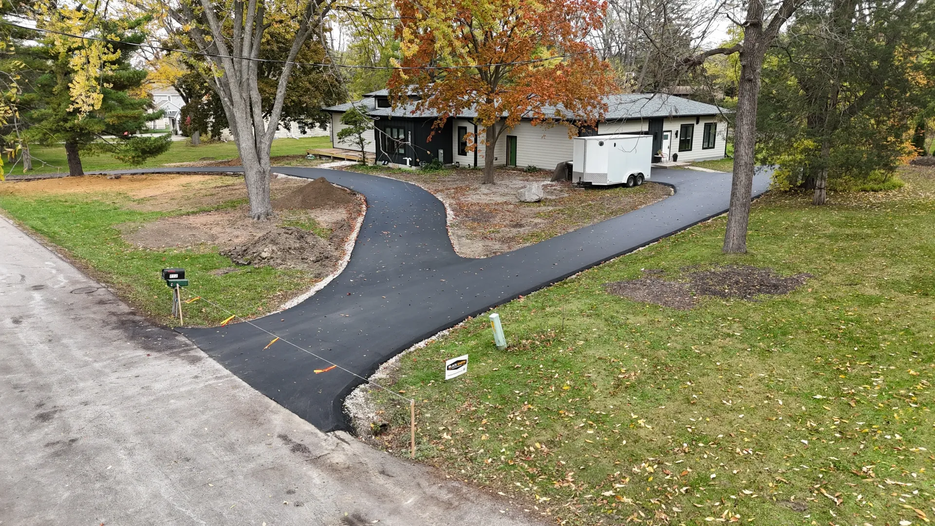 Curved black driveway leading to a house with autumn trees and a lawn in front